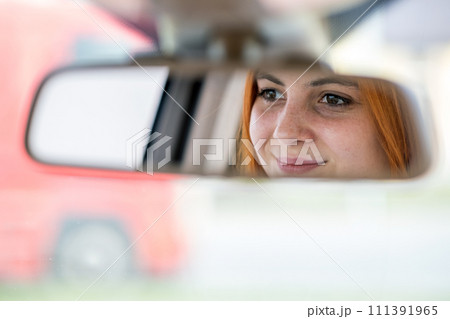 Young woman driver checking rear view mirror looking backwards while driving a car. Young woman driver checking rear view mirror looking backwards while driving a car. 111391965