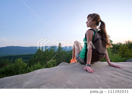 Hiker girl resting on rocky mountain top enjoying morning nature during her travel on wilderness trail. Lonely female traveler traversing high hilltop route. Healthy lifestyle concept 111392031