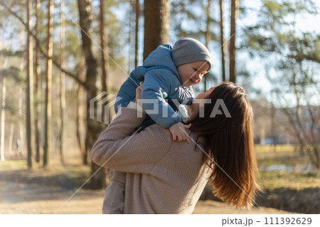 Happy family outdoor. Mother embracing her child outdoor. Mom lifting in air little toddler child son. Woman and little baby boy resting walking in park. Mother hugs baby with love care 111392629