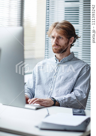Graphic vertical portrait of bearded adult man using computer at workplace in IT office against window Graphic vertical portrait of bearded adult man using computer at workplace in IT office against window 111393242