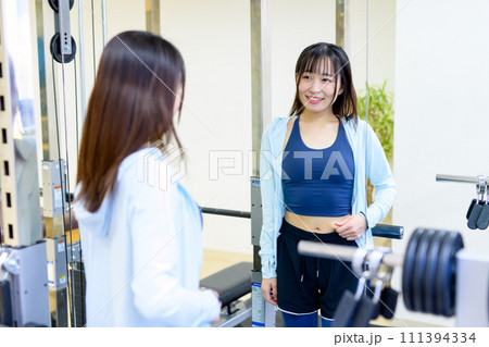 プライベートジムの鏡でお腹をつまみ体型をチェックする若い女性　パーソナルジム　筋トレ女子　個室 111394334