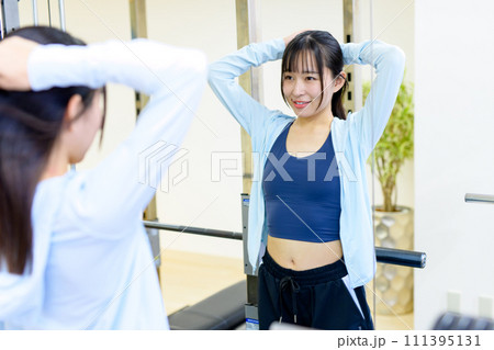 ジムの鏡で体型をチェックし準備する若い女性 プライベートジム 筋トレ女子 髪を結ぶ ジムの鏡で体型をチェックし準備する若い女性 プライベートジム 筋トレ女子 髪を結ぶ 111395131