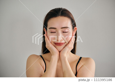 両手で顔をマッサージして肌のお手入れをする30代女性 111395186