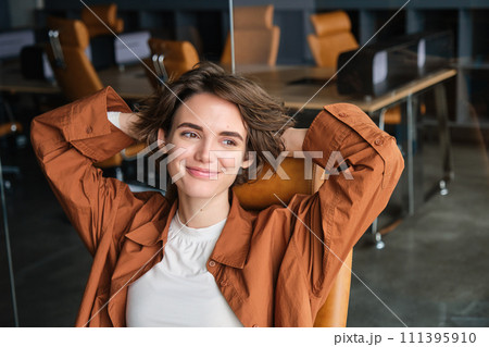 Close up portrait of woman at workplace, digital nomad sits back and relaxed in an office, resting after productive work day, smiling pleased 111395910