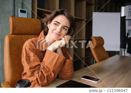 Close up portrait of young female entrepreneur, saleswoman in casual clothes, sitting in her office at the table and smiling 111396047