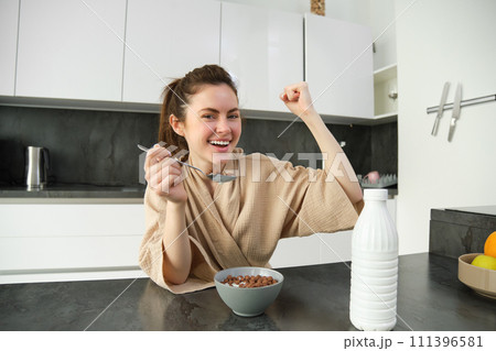 Portrait of happy, laughing young woman eating cereals with milk, triumphing, having breakfast and feeling excited, energetic morning concept Portrait of happy, laughing young woman eating cereals with milk, triumphing, having breakfast and feeling excited, energetic morning concept 111396581