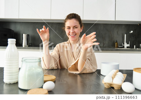 Attractive young cheerful girl baking at the kitchen, making dough, holding recipe book, having ideas 111396663