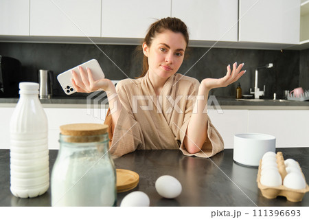Attractive young cheerful girl baking at the kitchen, making dough, holding recipe book, having ideas 111396693
