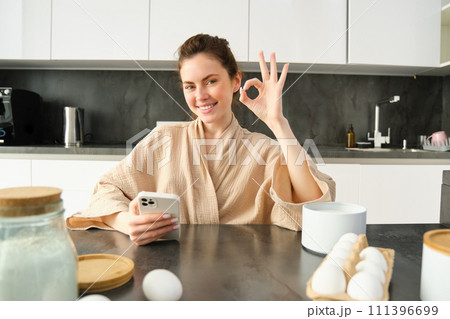 Attractive young cheerful girl baking at the kitchen, making dough, holding recipe book, having ideas Attractive young cheerful girl baking at the kitchen, making dough, holding recipe book, having ideas 111396699