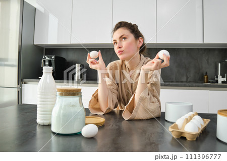 Attractive young cheerful girl baking at the kitchen, making dough, holding recipe book, having ideas Attractive young cheerful girl baking at the kitchen, making dough, holding recipe book, having ideas 111396777