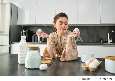 Attractive young cheerful girl baking at the kitchen, making dough, holding recipe book, having ideas Attractive young cheerful girl baking at the kitchen, making dough, holding recipe book, having ideas 111396779