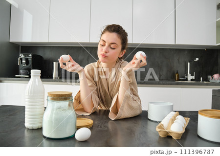Attractive young cheerful girl baking at the kitchen, making dough, holding recipe book, having ideas 111396787
