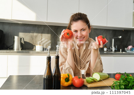 Portrait of beautiful woman cooking in the kitchen, chopping vegetables on board, holding tomatoes, lead healthy lifestyle with preparing fresh salads, vegan meals 111397045