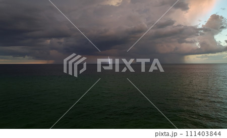 Dark stormy clouds forming on gloomy sky during heavy rainfall season over sea surface in evening Dark stormy clouds forming on gloomy sky during heavy rainfall season over sea surface in evening 111403844