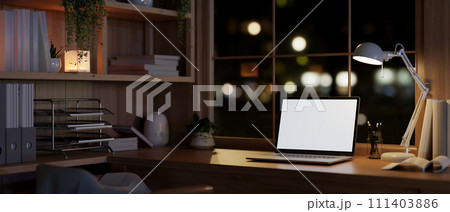 A modern, vintage, and cozy home office workspace at night with a white-screen laptop mockup. 111403886