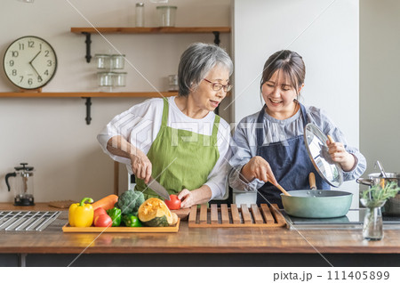家のキッチンで一緒に料理・家事・自炊をする笑顔のアジア人高齢者女性と若い女性（家政婦・家事代行） 111405899