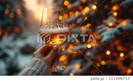 Hand holding a glass of sparkling wine against a snowy, festive background. 111406717