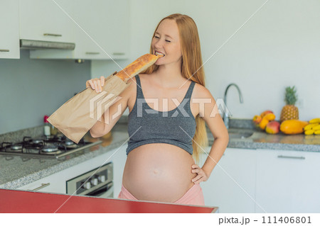Pregnant woman eating bread in the kitchen. Exploring the impact of gluten during pregnancy: understanding the potential benefits and risks for maternal health and fetal development 111406801