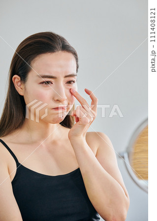 鏡を見ながら目元のシワを気にする30代女性 鏡を見ながら目元のシワを気にする30代女性 111408121