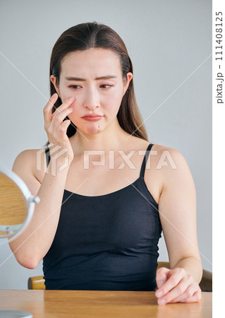 鏡を見ながら目元のシワを気にする30代女性 111408125