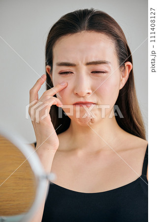 鏡を見ながら目元のシワを気にする30代女性 111408127