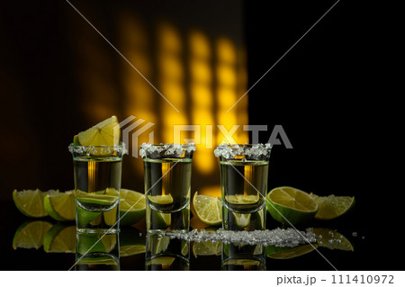 Tequila with sea salt and lime slices on a black reflective background. 111410972