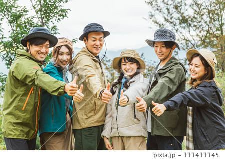 秋冬のキャンプ場で仲間と一致団結してサムズアップする男女（友情・友達・チームワーク・アウトドア） 111411145