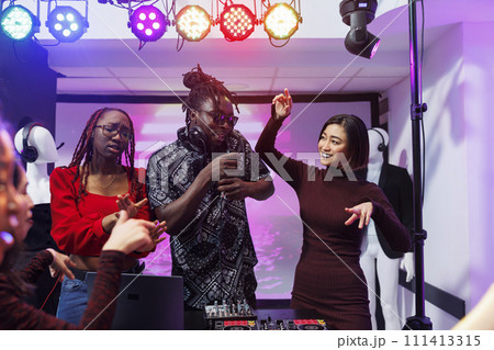 Band frontman singing and diverse women dancing on stage at discotheque in nightclub. Carefree musicians using dj station and microphone while performing at club disco party Band frontman singing and diverse women dancing on stage at discotheque in nightclub. Carefree musicians using dj station and microphone while performing at club disco party 111413315