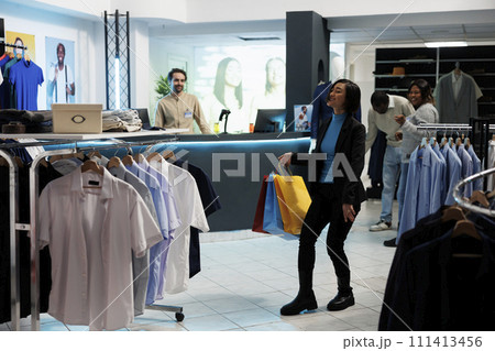 Clothing store happy satisfied buyer carrying bags of purchased apparel and dancing. Cheerful asian woman shopaholic holding paper packages and dancing in department mall Clothing store happy satisfied buyer carrying bags of purchased apparel and dancing. Cheerful asian woman shopaholic holding paper packages and dancing in department mall 111413456