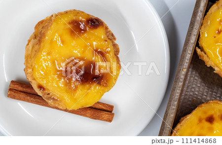 Pastel de nata tarts or Portuguese egg tart and cinnamon sticks isolated on white background. Pastel de Belem is a small pie with a crispy puff pastry crust and a custard cream filling 111414868
