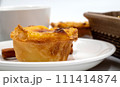 One Pastel de nata or Portuguese egg tart on a white plate. Pastel de Belm is a small pie with a crispy puff pastry crust and a custard cream filling 111414874