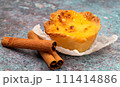 One Pastel de nata or Portuguese egg tart and cinnamon sticks. Pastel de Belm is a small pie with a crispy puff pastry crust and a custard cream filling 111414886