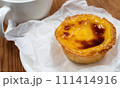 One Pastel de nata or Portuguese egg tart on a white plate. Pastel de Belm is a small pie with a crispy puff pastry crust and a custard cream filling 111414916