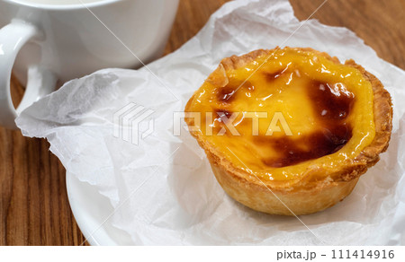 One Pastel de nata or Portuguese egg tart on a white plate. Pastel de Belm is a small pie with a crispy puff pastry crust and a custard cream filling One Pastel de nata or Portuguese egg tart on a white plate. Pastel de Belm is a small pie with a crispy puff pastry crust and a custard cream filling 111414916