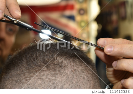 The hairdresser removes small hair from the client's head with scissors. 111415528