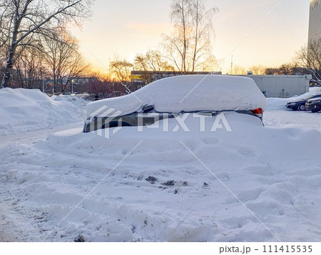 A snow-covered car in a parking lot against the background of the dawn sky.  111415535