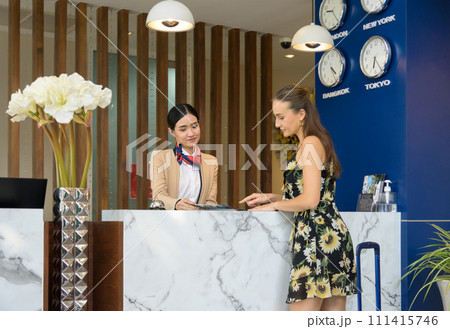 Female receptionist giving hotel information to woman traveller at check in counter. Female receptionist giving hotel information to woman traveller at check in counter. 111415746