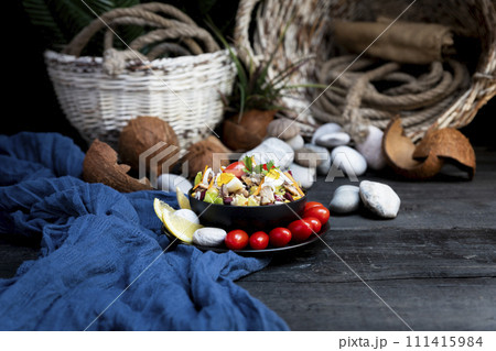 Fish salad with sardines, harringe, tuna, tomato, lemon, lettuce, cabbage, olives, beans, corn, carrotes and eggs on rustic kitchen table 111415984