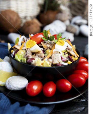 Fish salad with sardines, harringe, tuna, tomato, lemon, lettuce, cabbage, olives, beans, corn, carrotes and eggs on rustic kitchen table 111415988