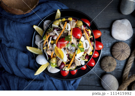 Fish salad with sardines, harringe, tuna, tomato, lemon, lettuce, cabbage, olives, beans, corn, carrotes and eggs on rustic kitchen table. Fresh and delicous seafood. Top view photo 111415992
