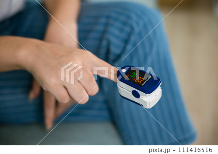 Young woman finger inserted into the pressure oximeter to assess health under sofa in living room at home, Self healthcare with corona virus pandemic, medical health care concept Young woman finger inserted into the pressure oximeter to assess health under sofa in living room at home, Self healthcare with corona virus pandemic, medical health care concept 111416516