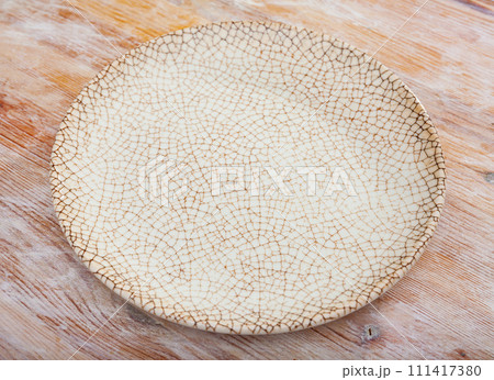 Empty hand-crafted ceramic plate on wooden table surface 111417380