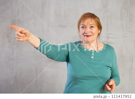 Amiable elderly woman in teal jumper pointing towards 111417952