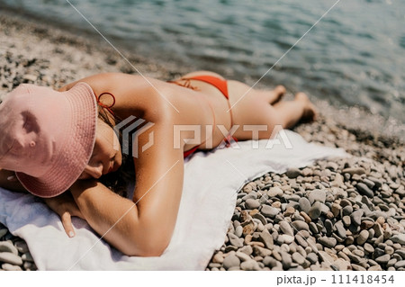 A woman sunbathes on the beach, lying on her stomach in a red swimsuit against the sea backdrop. A woman sunbathes on the beach, lying on her stomach in a red swimsuit against the sea backdrop. 111418454