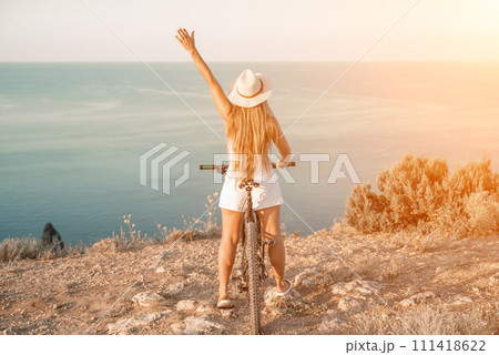 Woman travel bike sea. Happy woman cyclist sitting on her bike, enjoying the beautiful mountain and sea landscape, signifying the idea of an adventurous bike ride. 111418622