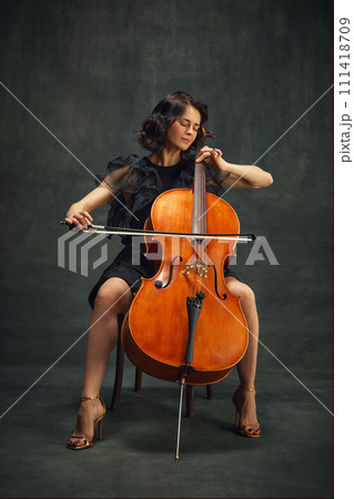 Cellist, elegant woman in deep concentration, playing cello passionately with eyes closed against vintage green background. 111418709