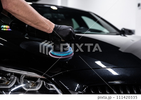Car detailing worker polishing black car body 111420335