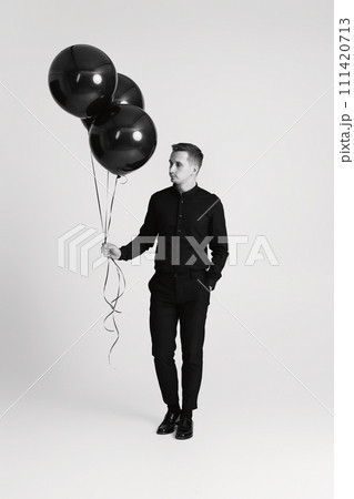 elegant caucasian man with bunch of black air balloons on white background. black and white elegant caucasian man with bunch of black air balloons on white background. black and white 111420713