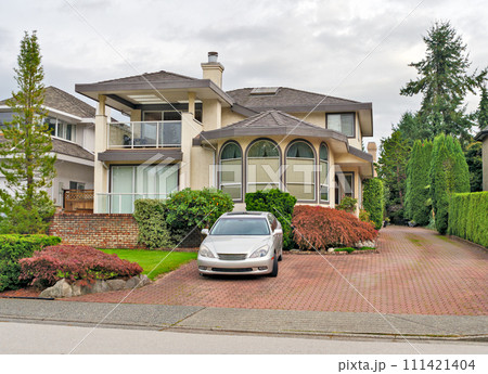 Big residential house with a car parked on pawed drvieway in front Big residential house with a car parked on pawed drvieway in front 111421404