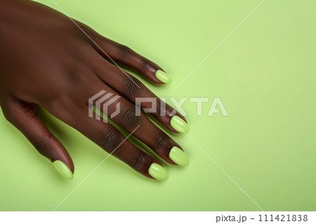 African American womans hand with long nails and green color manicure against green background 111421838